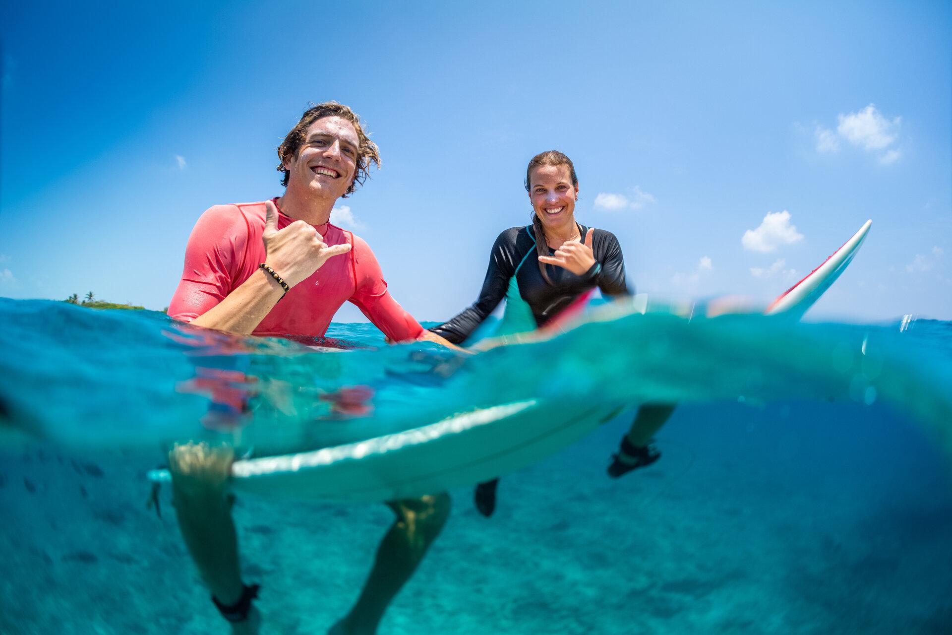Junge glückliche Surfer, Mann und Frau, sitzen auf den Surfbrettern im Wasser
