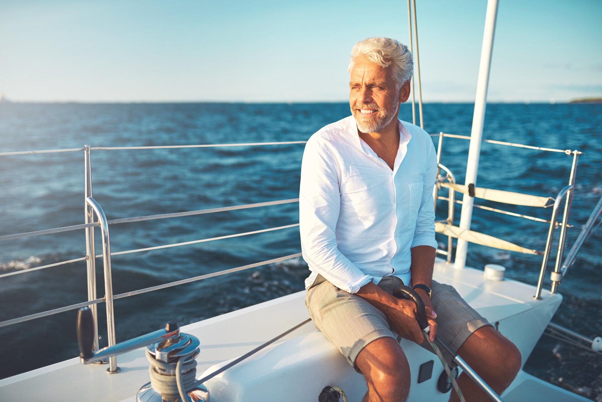 Lächelnder reifer Mann beim Segeln auf seiner Yacht an einem sonnigen Tag