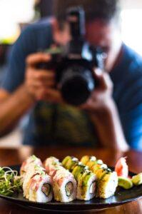 Menschen, Freizeit, Essen, Essen und Technik - Nahaufnahme eines Mannes mit Kamera, der ein Foto von Sushi im Restaurant macht.