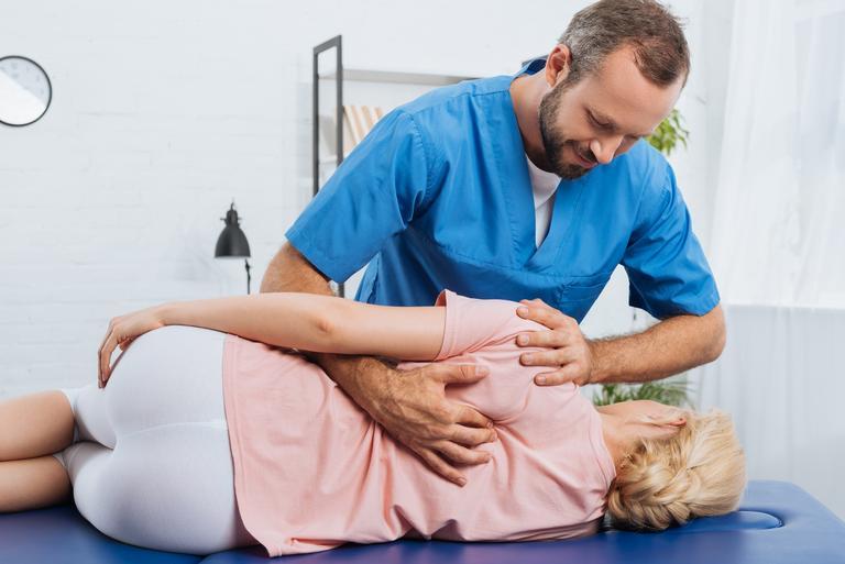 Porträt eines lächelnden Chiropraktikers, der den Rücken eines Patienten massiert, der auf einem Massagetisch im Krankenhaus liegt
