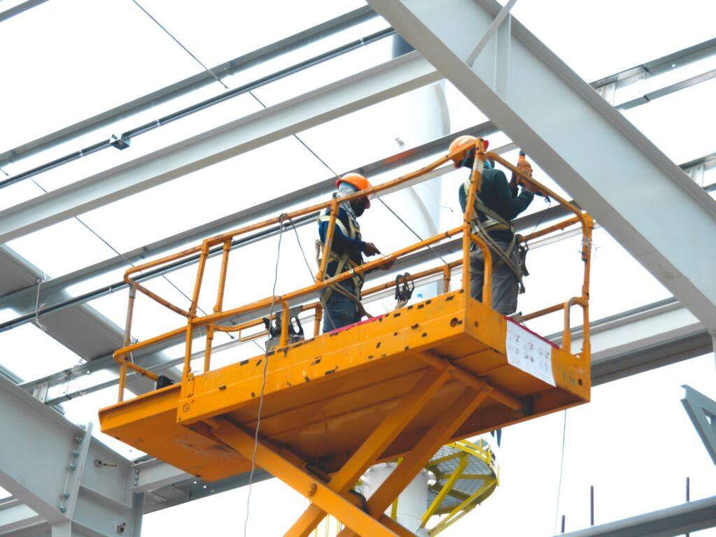 Arbeiter installieren Beleuchtungskörper in einem riesigen Industrielager mit einer hydraulischen Scherenhebebühne. MEP-Arbeiten auf einer Baustelle.