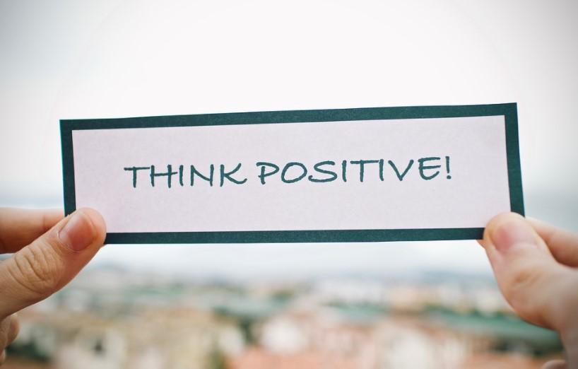 Zwei Hände halten ein Schild mit der Aufschrift "Think Positive!" hoch. Das Bild symbolisiert die Bedeutung einer positiven Denkweise für persönlichen und beruflichen Erfolg.