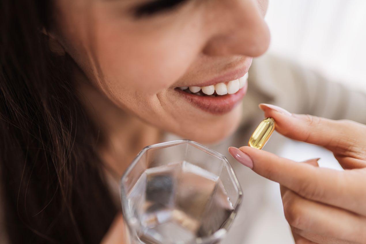 Nahaufnahme einer Frau, die eine Omega-3 Algenöl Kapsel mit einem Glas Wasser einnimmt