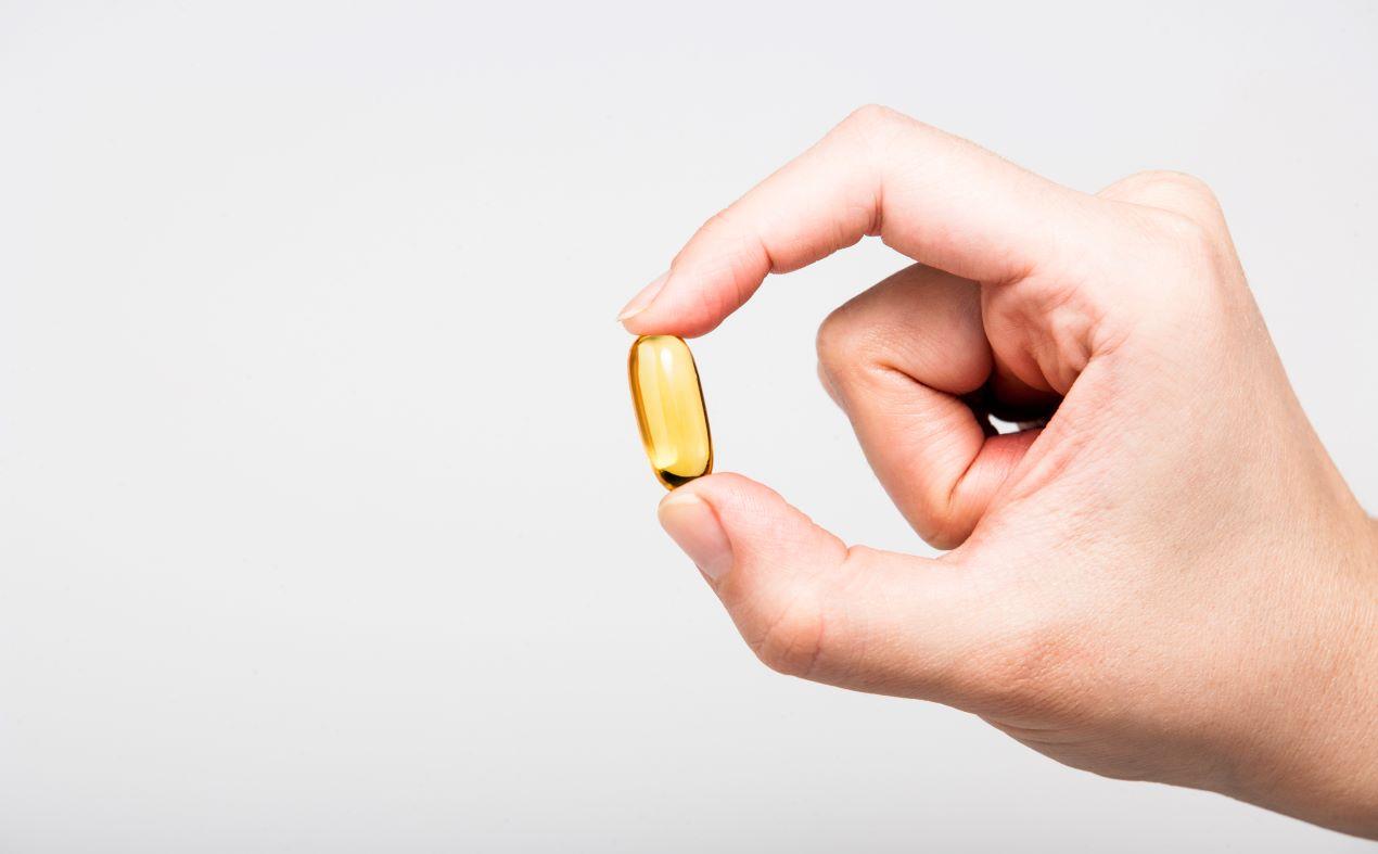 Nahaufnahme einer Hand, die eine Omega-3 Algenöl Kapsel zwischen den Fingern hält