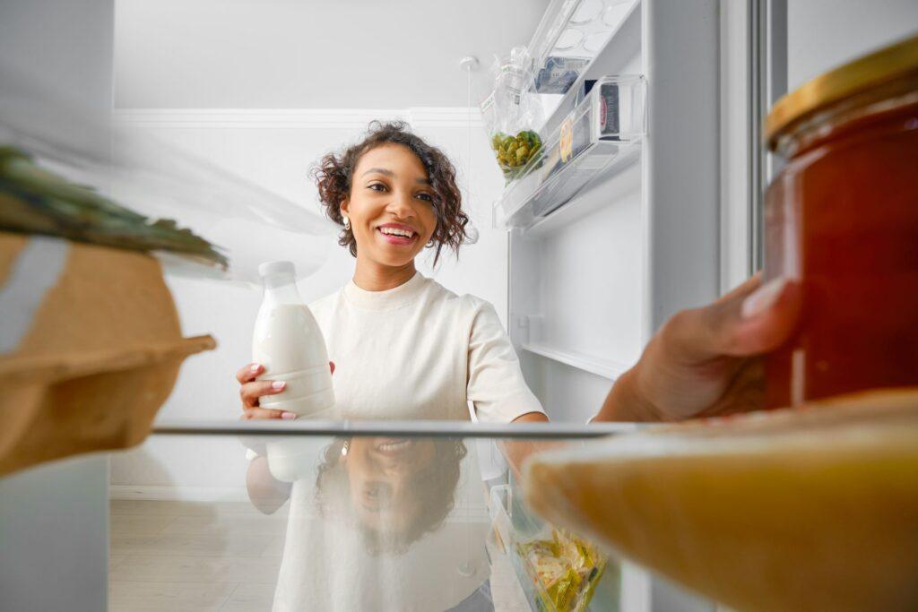 Junge Frau öffnet Kühlschrank und nimmt Milch heraus.