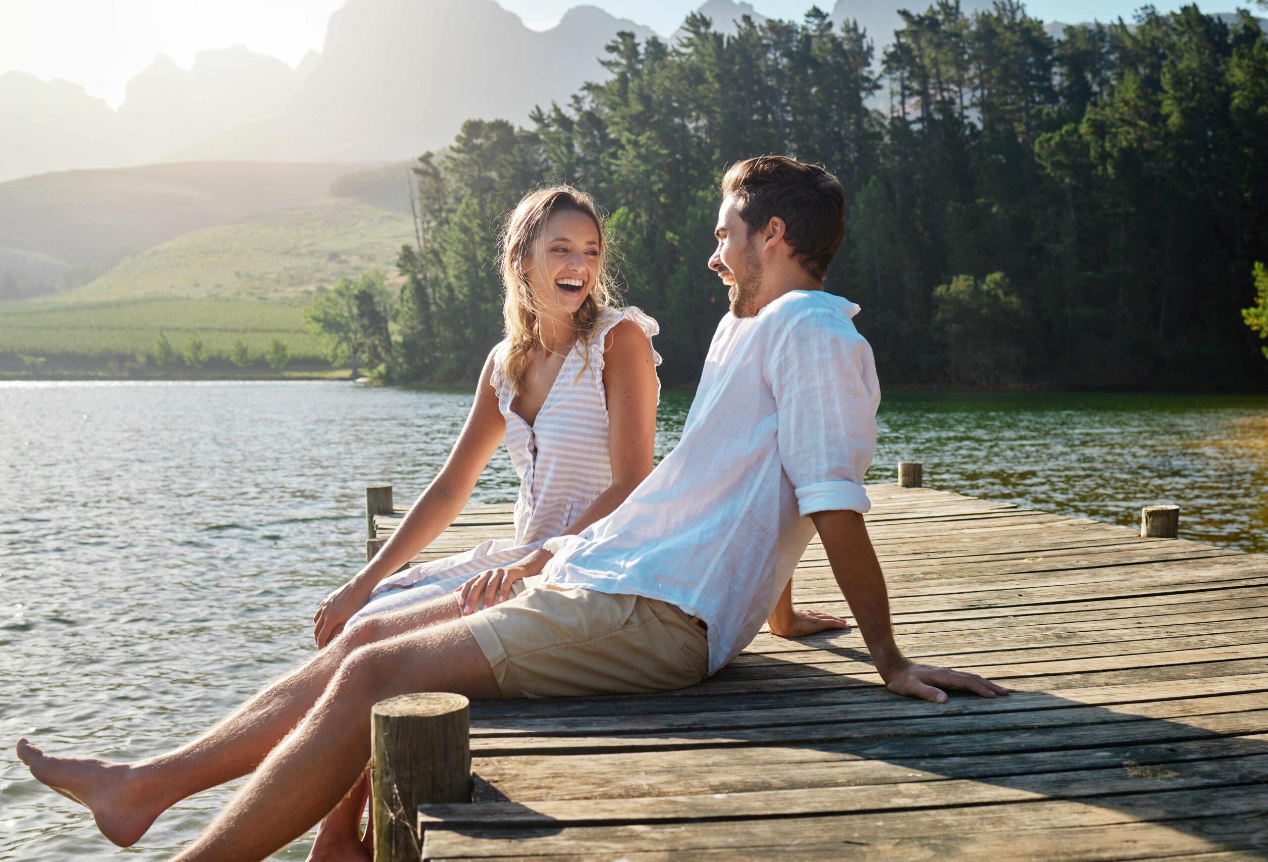 Liebe, lachen und am Ufer des Sees mit einem Paar für Bindung, Romantik und ein liebevolles Date.