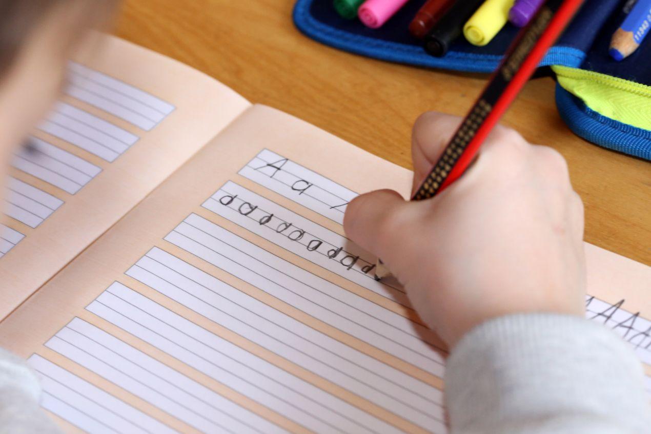 Kind schreibt Buchstaben in ein Heft waehrend des Unterrichts an einer bilingualen grundschule berlin